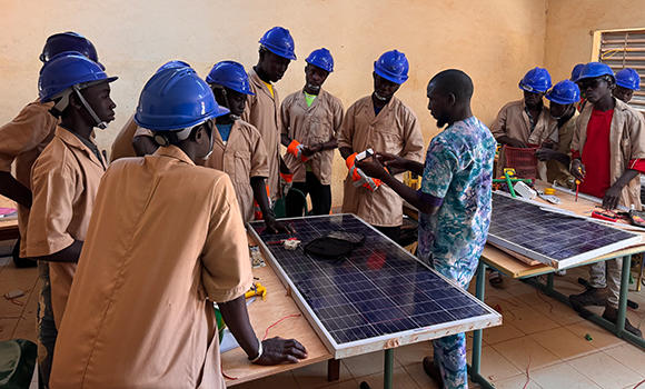 Ein Lehrer und Berufschüler*innen stehen um zwei Tische, auf denen Solarpanelen liegen.
