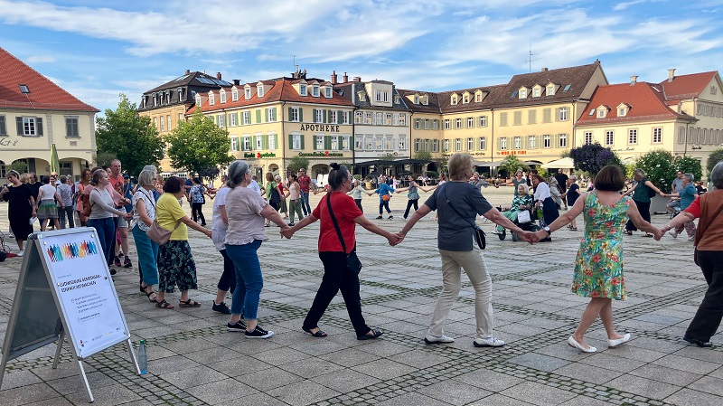 Auf dem Marktplatz tanzen Menschen in einem Kreis gemeinsam