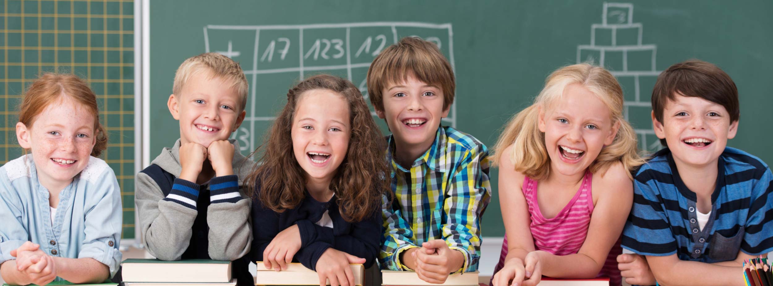 Lachende Schülerinnen und Schüler vor einer Tafel