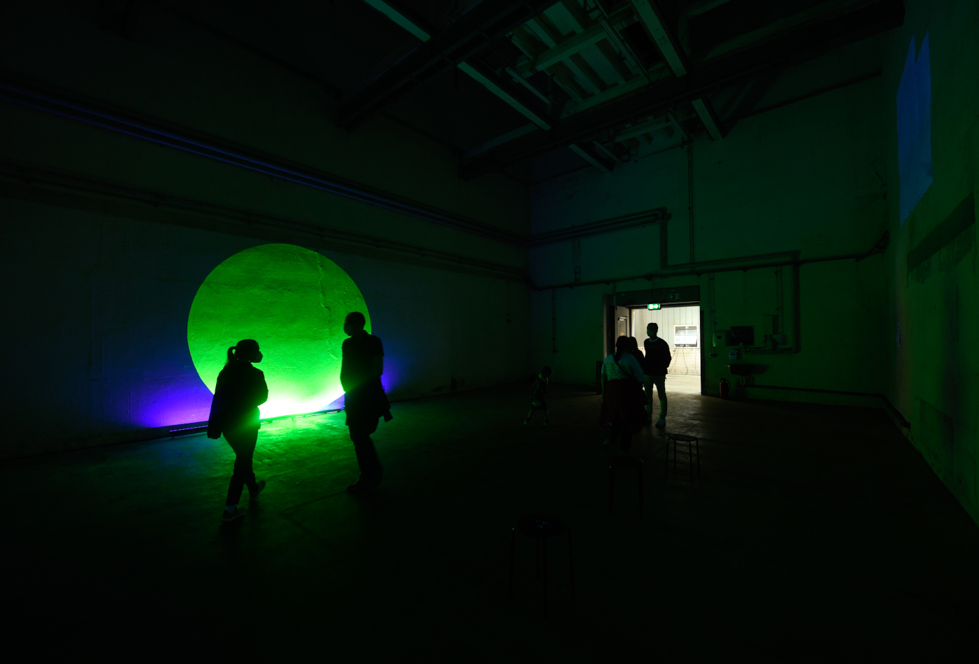 Einige Menschen stehen in einem dunklen Raum vor einem hell leuchtenden gelben Kreis - eine Arbeit der Künstlerin Karima Klasen.