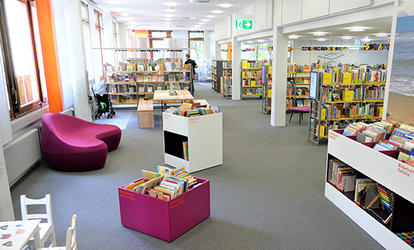 Ein Blick in die Kinderbücherei der Stadtbibliothek. Das Bild zeigt Bücherregale, Bücherkisten und verschiedene Sitzmöglichkeiten.
