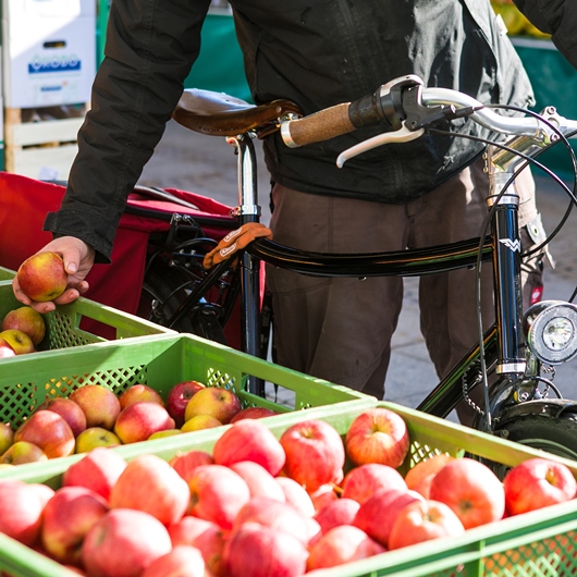 Mann mit Fahrrad kauft Äpfel am Marktstand