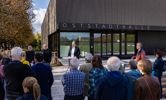 Oberbürgermeister Dr. Matthias Knecht steht an einem Stehtisch vor der Oststadthalle. Mehrere Menschen hören zu.