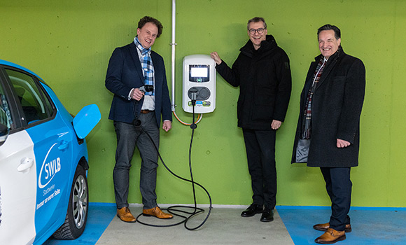 OB Matthias Knecht, Alexander Lahl und Christian Schneider in der Rathausgarage neben einem Ladepunkt und einem E-Auto.