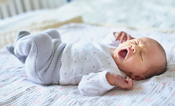 Baby liegt auf dem Rücken und gähnt.