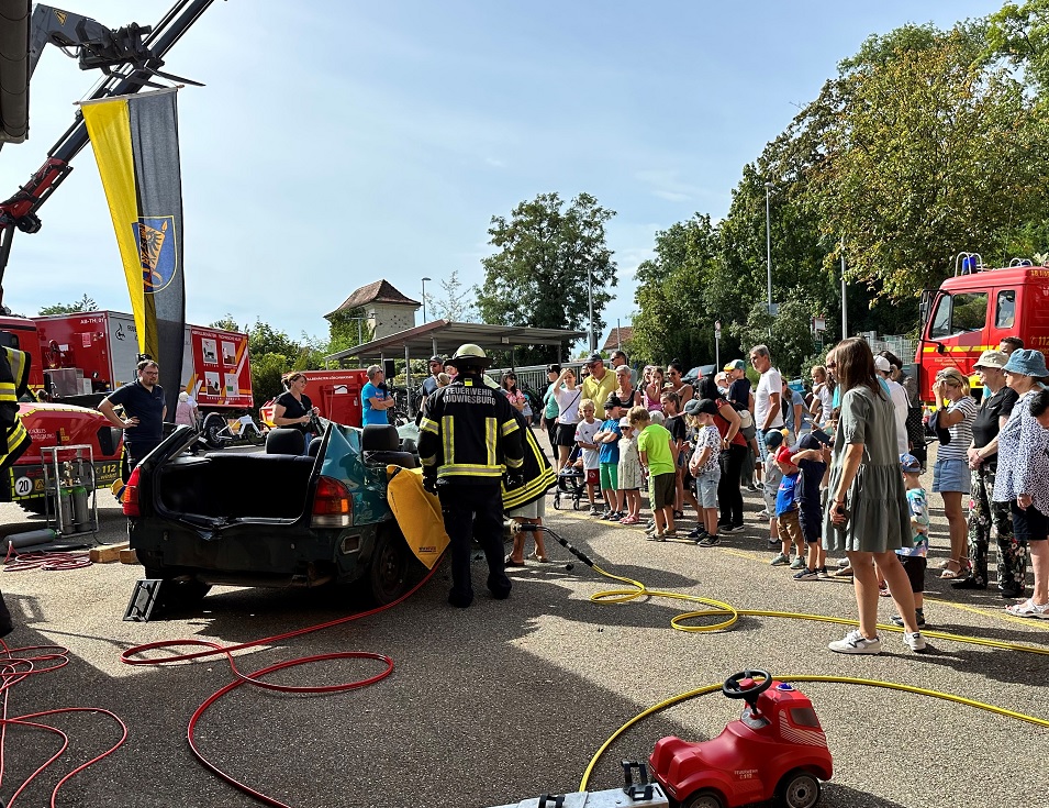 Bei einer Vorführung im Rahmen des Tags der offenen Tür stehen Feuerwehrleute rund um ein demoliertes Auto. Mehrere Zuschauer beobachten die Aufführung.