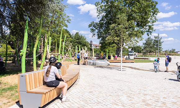 Platz mit Bänken, einem Wasserspiel und einem Spielplatz.