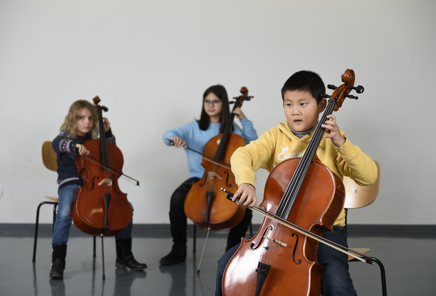 Ein Junge und zwei Mädchen spielen Cello.