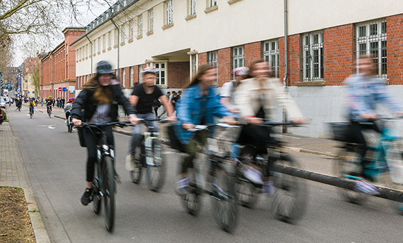 Im Vordergrund fahren sechs Menschen dicht beieinander auf dem Rad in der Alleenstraße. Im Hintergrund befinden sich weitere Radfahrende
