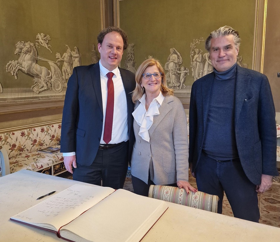 Drei Menschen stehen in einem Raum mit prunkvollen Wänden. Vor ihnen ein Tisch mit dem aufgeschlagenen Goldenen Buch der Stadt Bergamo.