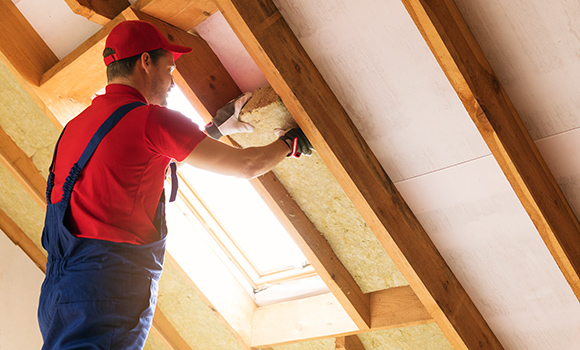 Handwerker in Arbeitskleidung dämmt von innen ein Dach.