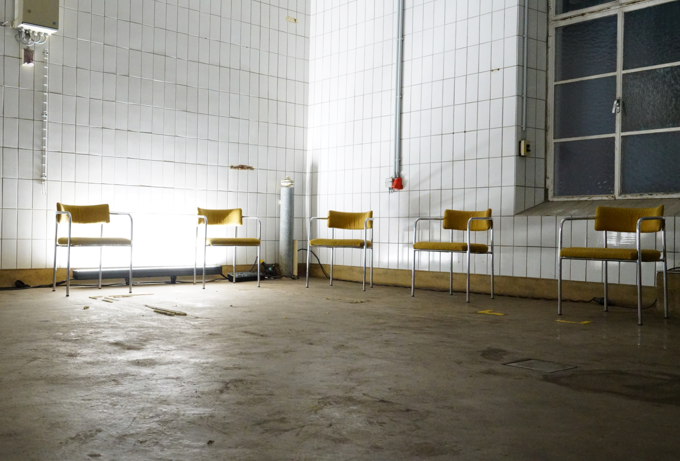 Unbesetzte Stühle stehen im Halbkreis in einem gekachelten Raum.