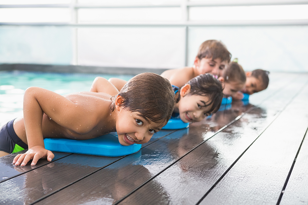 Fünf Kinder lehnen sich auf Schwimmbrettern aus dem Schwimmbecken.