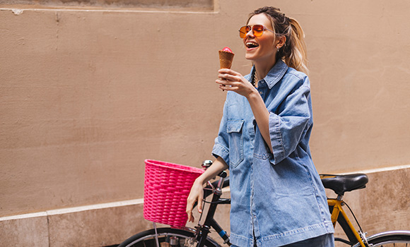 Frau schiebt mit der einen Hand ihr Fahrrad. In der anderen Hand hält sie ein Eis in der Waffel.