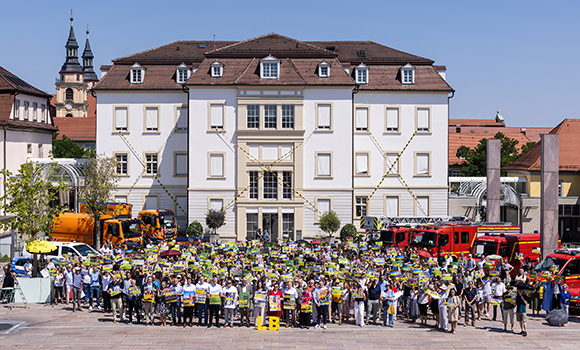 Mehrere hundert Menschen stehen mit Plakaten vor dem Rathaus. Das Rathaus ist mit Absperrbändern markiert. Auf dem Rathaushof stehen außerdem Fahrzeuge der Feuerwehr und der Technischen Dienste.