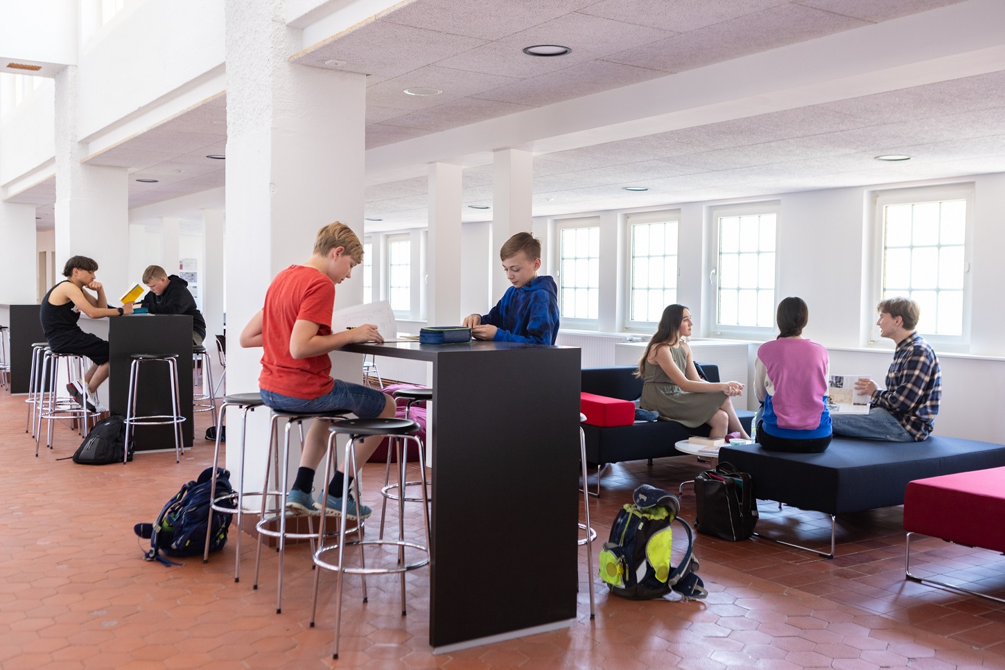 Eine Gruppe von Studierenden in einem modernen, gut beleuchteten Studienbereich mit großen Fenstern, Tischen und Stühlen.