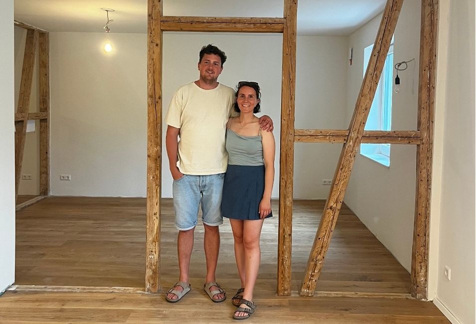 Fröhliches junges Paar auf einer Baustelle im Inneren eines alten Hauses mit freigelegtem Fachwerk.