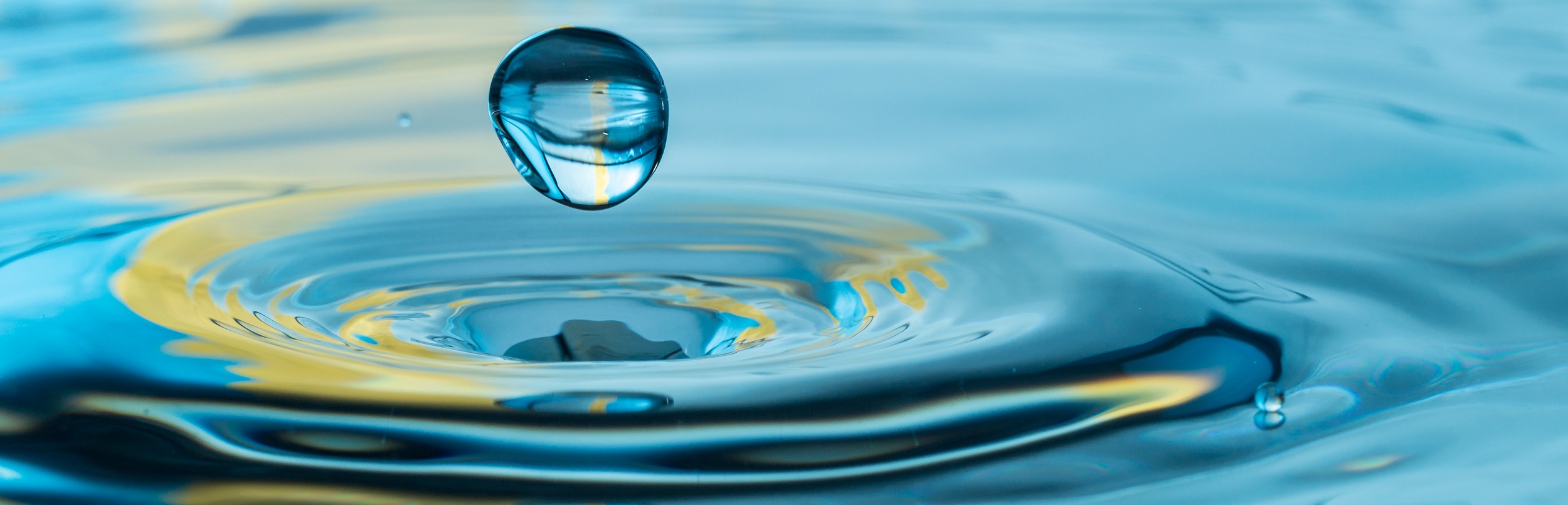 Wassertropfen prallt auf die Wasseroberfläche und löst kleine Wellen aus