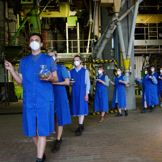 Menschen mit blauen Kitteln laufen durch die Produktionshalle.