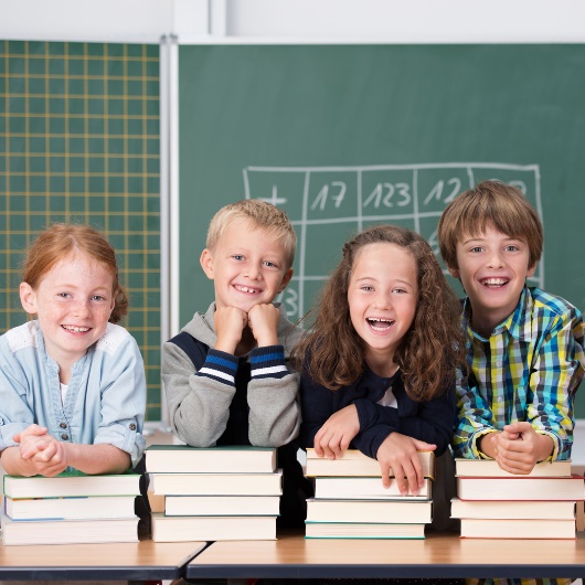 Kinder stehen lachend nebeneinander im Klassenzimmer, im Hintergrund eine Schultafel