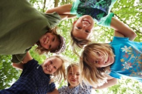 Fünf Kinder stehen im Kreis und schauen nach unten. Der Hintergrund zeigt grünes Laub.