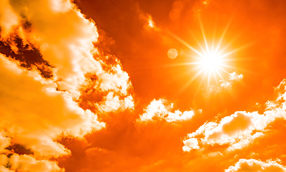 Gleißende Sonne am Himmel mit ein paar Wolken.