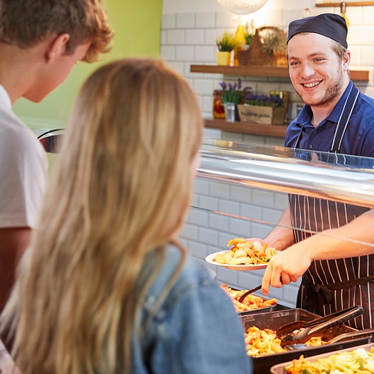 Koch teilt Essen an Schüler*innen aus – Link zur Seite Betreuung und Mittagessen