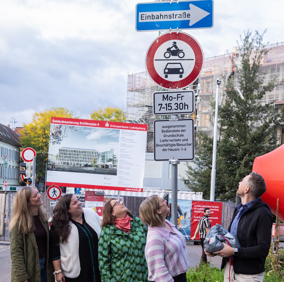 Ein Mann und vier Frauen blicken nach oben auf mehrere Verkehrszeichen. 