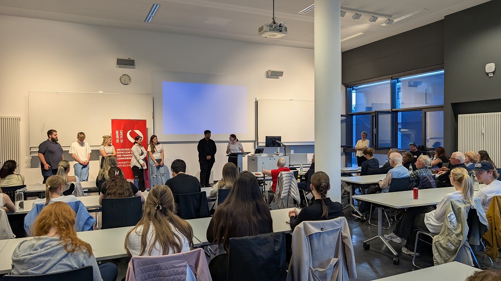 Mehrere Personen stehen vor Publikum in einem Hörsaal.