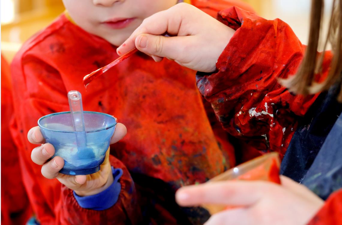 Ein Kind beim Farbmischen mit einem blauen Becher