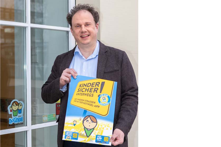 Ein Mann steht vor einer Glastür mit einem Plakat in den Händen. Auf der Glastür Aufkleber der Notinsel.
