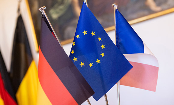 Das Bild zeigt von links nach rechts die Flaggen von Deutschland, der Europäischen Union und Frankreich.