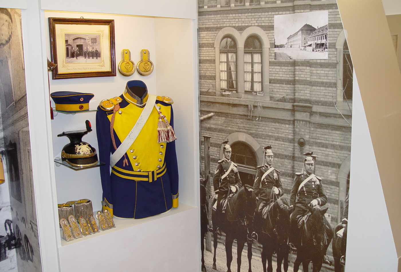 Eine Uniform steht in einem Schaukasten, daneben ein historisches Foto berittener Soldaten