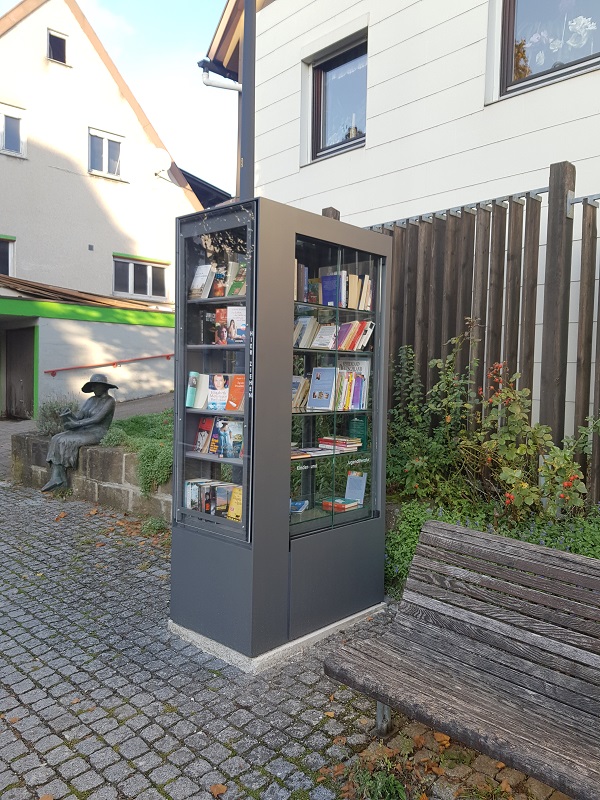 Bücherschrank voller Bücher zwischen Statue und Sitzbank