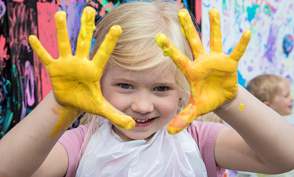 Mädchen zeigt seine gelb angemalten Hände.