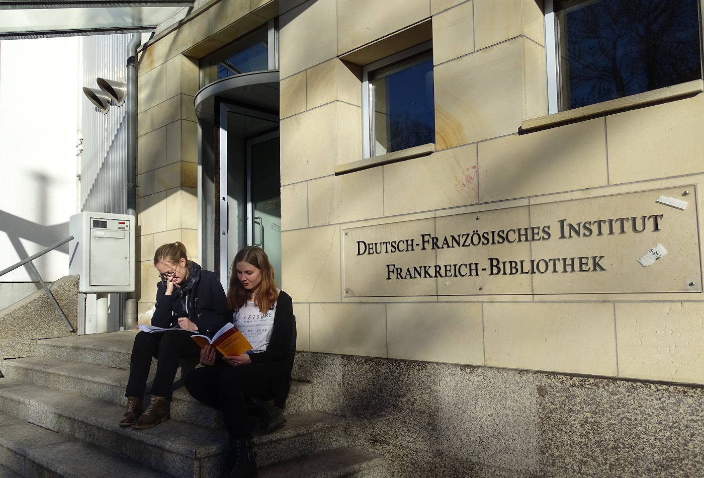 Zwei junge Frauen sitzen auf den Stufen zum Eingang des Deutsch-Französischen Institutes