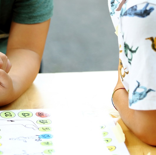 Zwei Jugendliche sitzen am Tisch und spielen ein Brettspiel (eine Ralley)